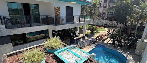 A modern two-story building with a rooftop terrace, a swimming pool, and outdoor seating.