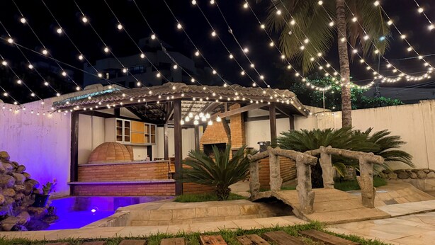 A patio area with string lights, a brick oven, and a small pool. - Santa Rita Pousada (Guarujá)