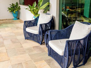 Two wicker chairs with white cushions on a tiled floor.