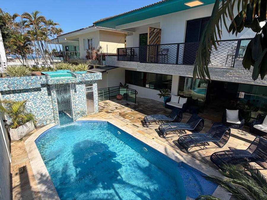 Piscina com espreguiçadeiras, um alpendre coberto e um edifício com varanda.