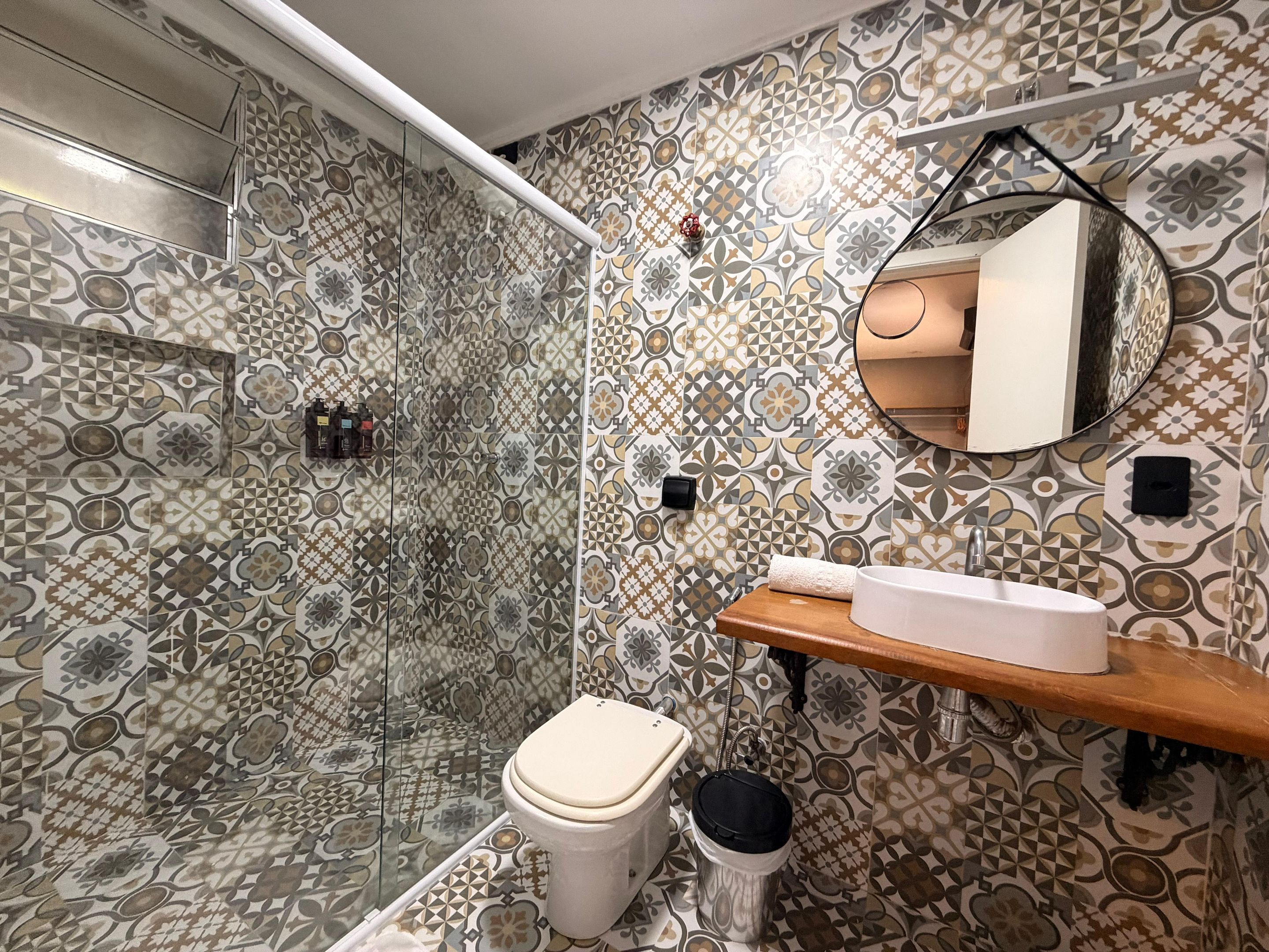 A bathroom with patterned tiles, a toilet, a sink, a mirror, and a shower area.