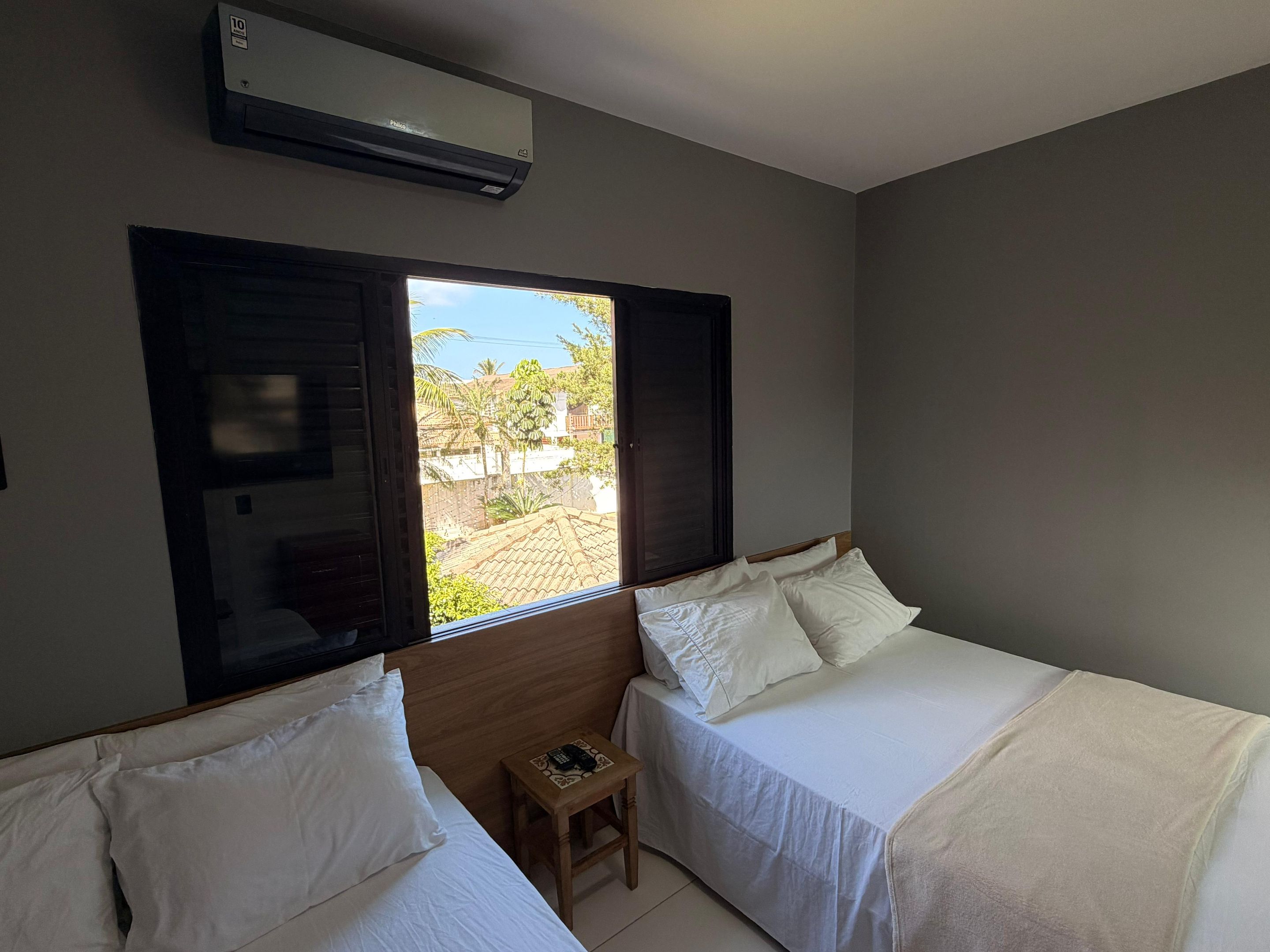 Habitación de hotel con dos camas, una mesita, una ventana con contraventanas y un equipo de aire acondicionado.