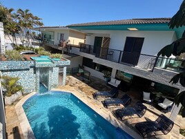 Une piscine avec des chaises longues, une petite cascade et un bâtiment doté d’un toit en tuiles et de balcons.