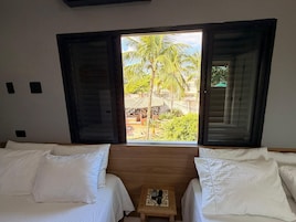 A room with two beds, a small table with a remote control, and a window with an open shutter.
