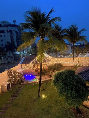 A pool area with string lights, palm trees, and a building in the background.
