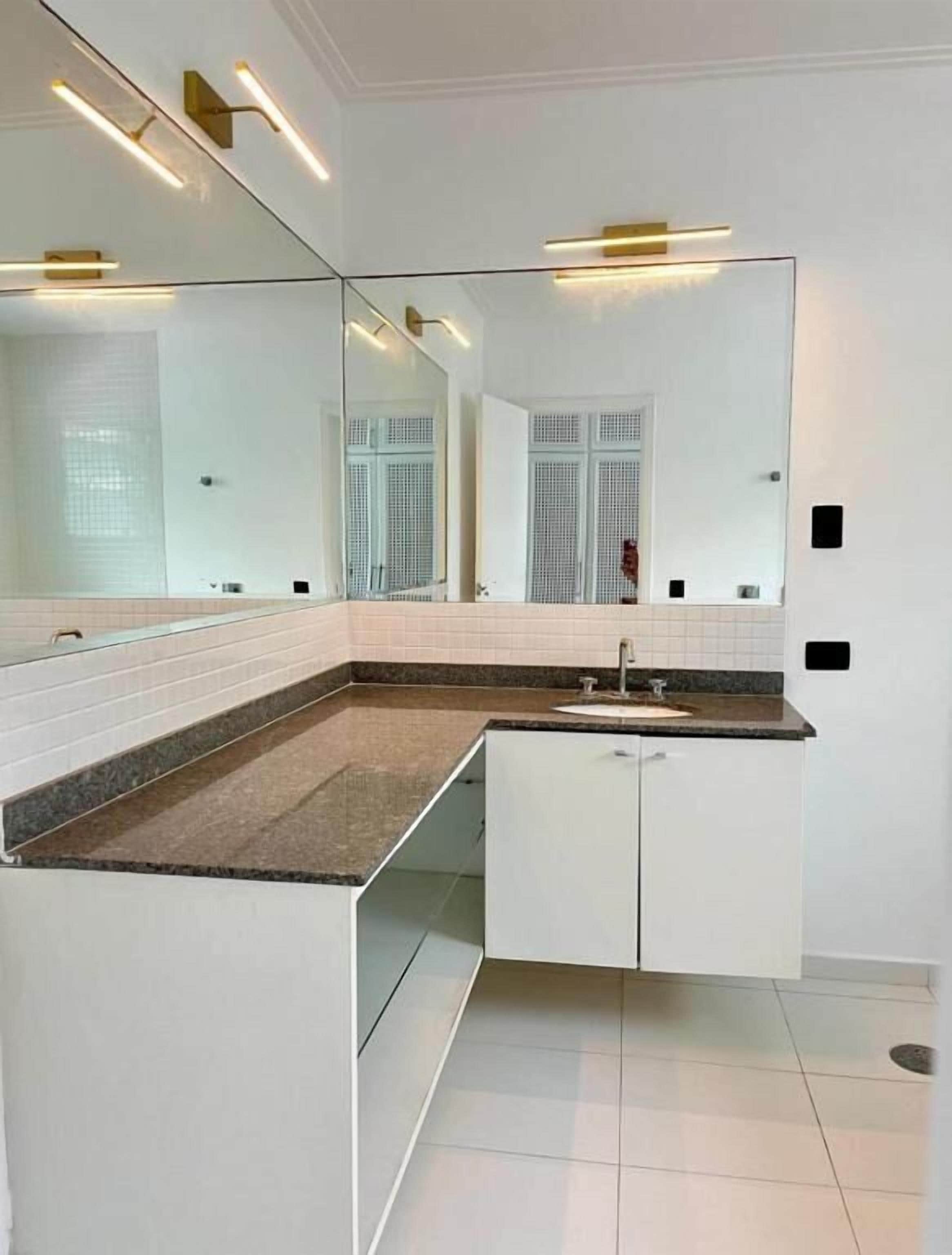 A modern bathroom with a large mirror, white cabinetry, and a granite countertop.