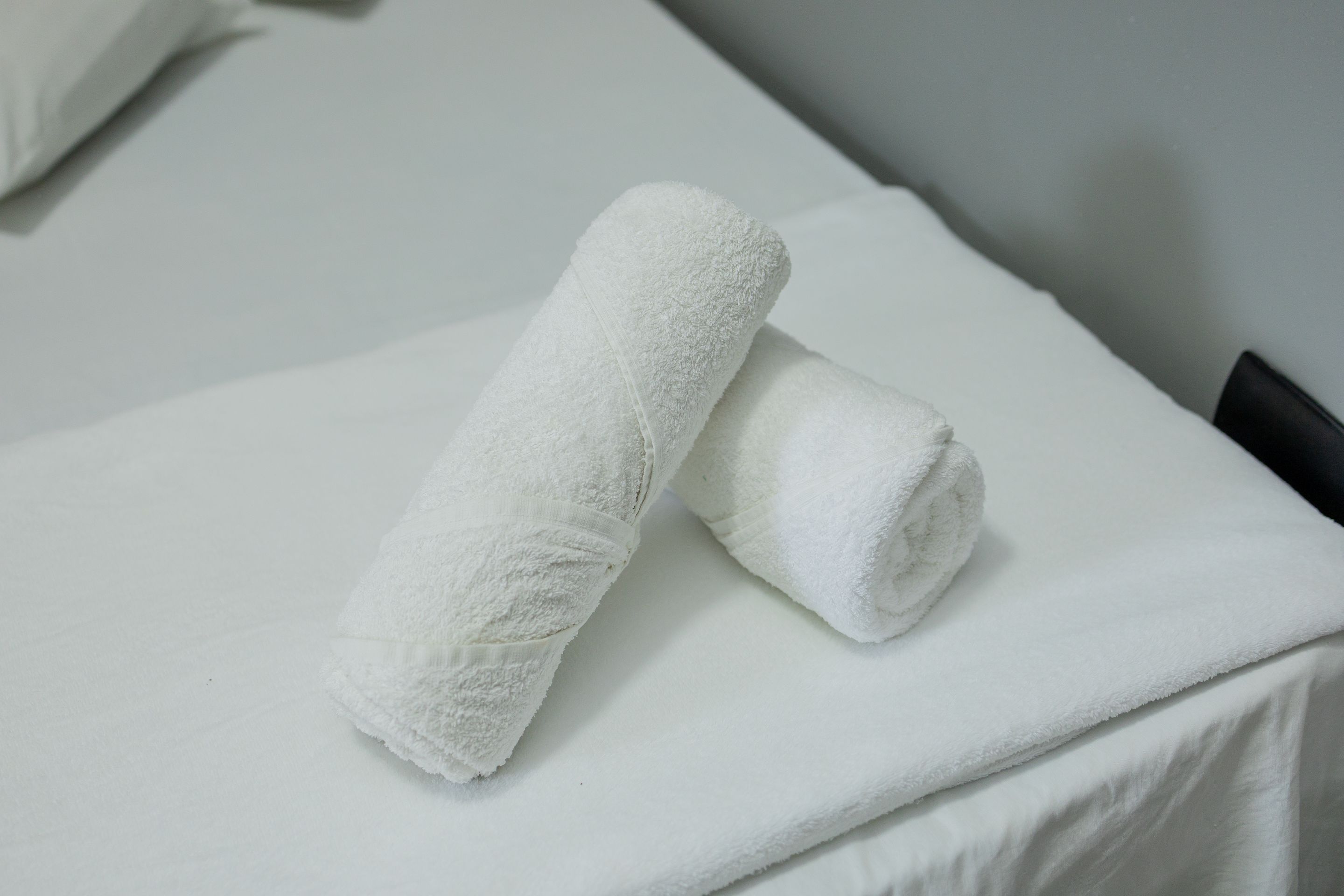 A bed with white linens and two rolled towels.