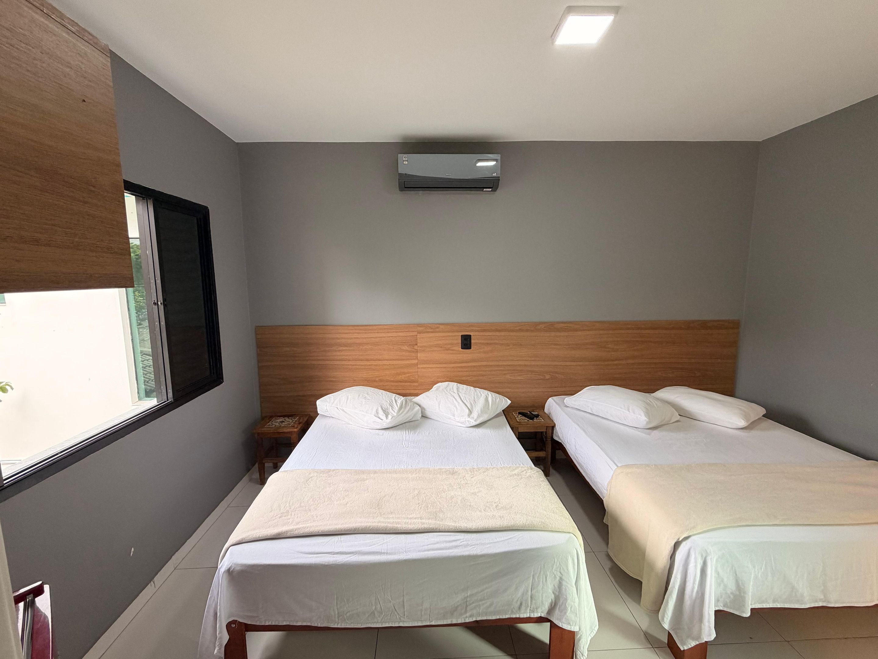 A hotel room with two beds, a window, an air conditioning unit, and a wooden headboard.
