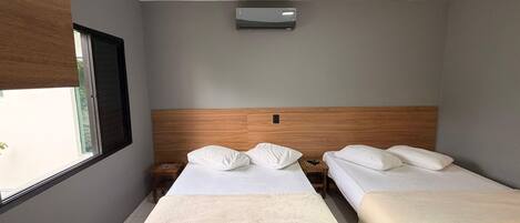 A hotel room with two beds, a window, an air conditioning unit, and a wooden headboard.