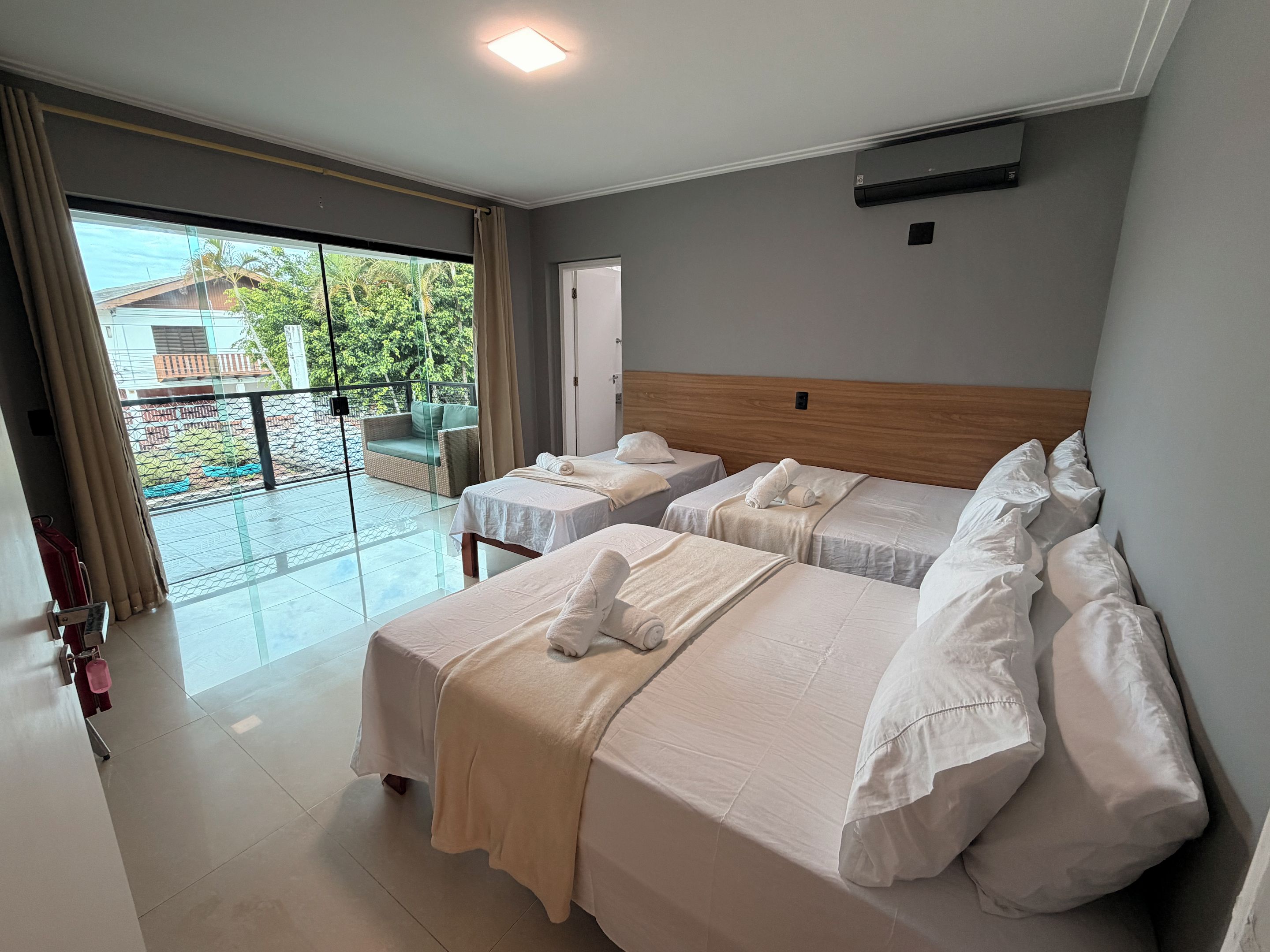A hotel room with two beds, a balcony with a view of greenery, and a sliding glass door.