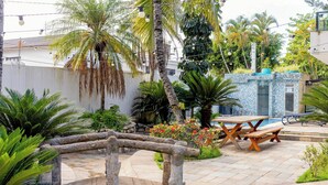 A patio area with a stone bridge, a picnic table, and various tropical plants. - Santa Rita Pousada (Guarujá)
