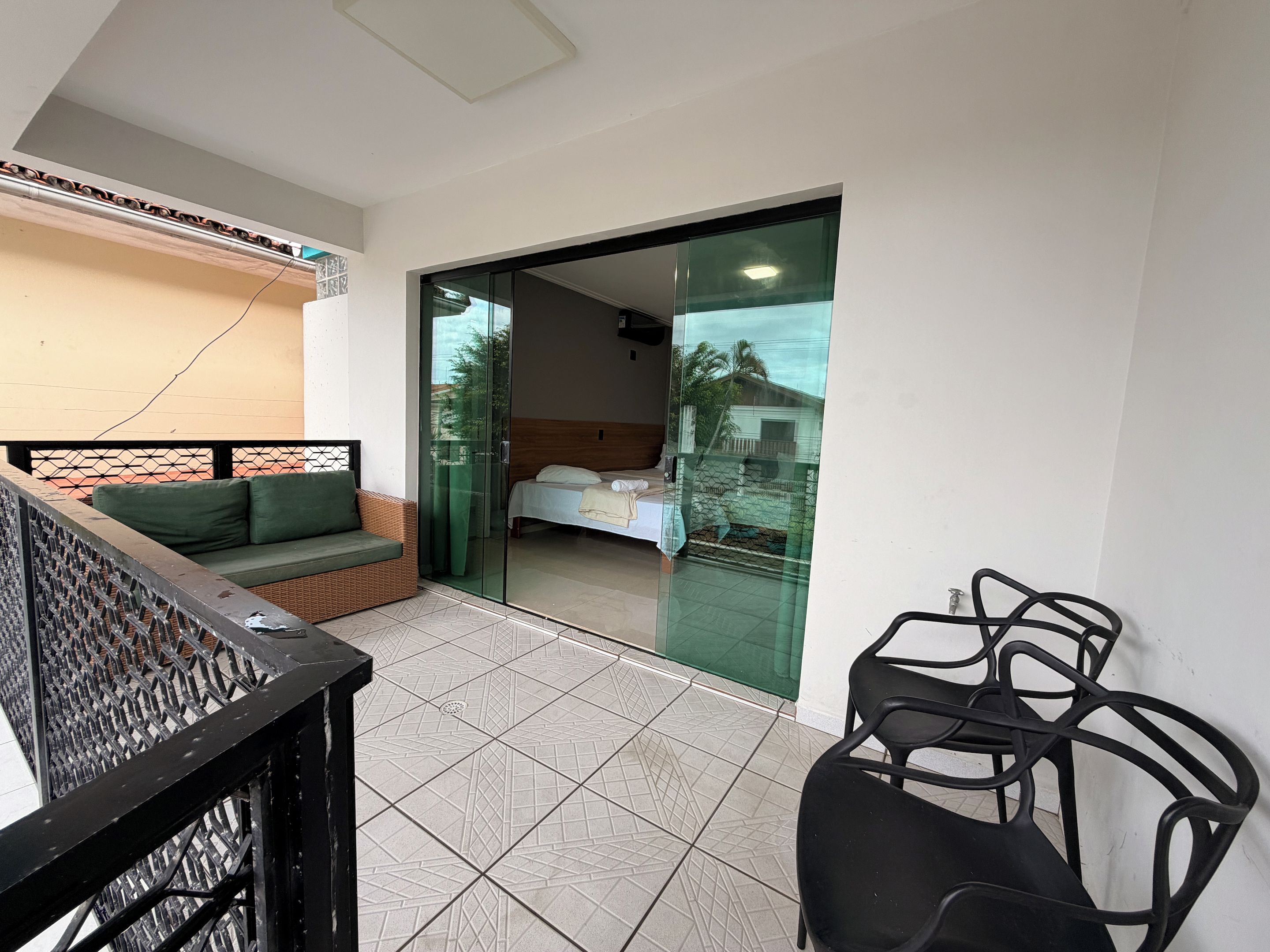 A balcony with a sofa, a chair, and a bed visible through a glass door.