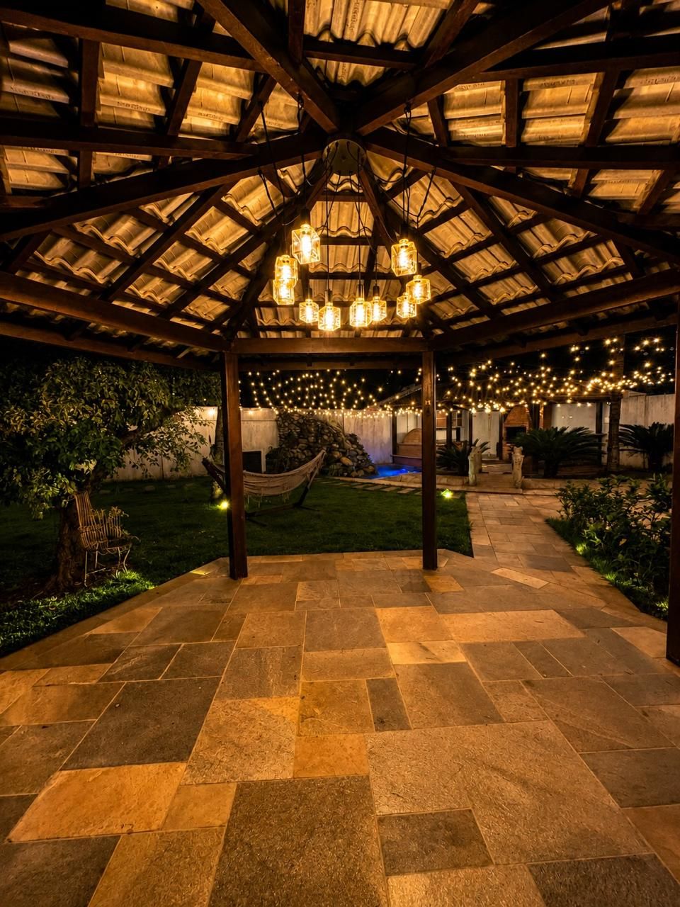 A covered outdoor area with a stone floor, wooden beams, and hanging lanterns.