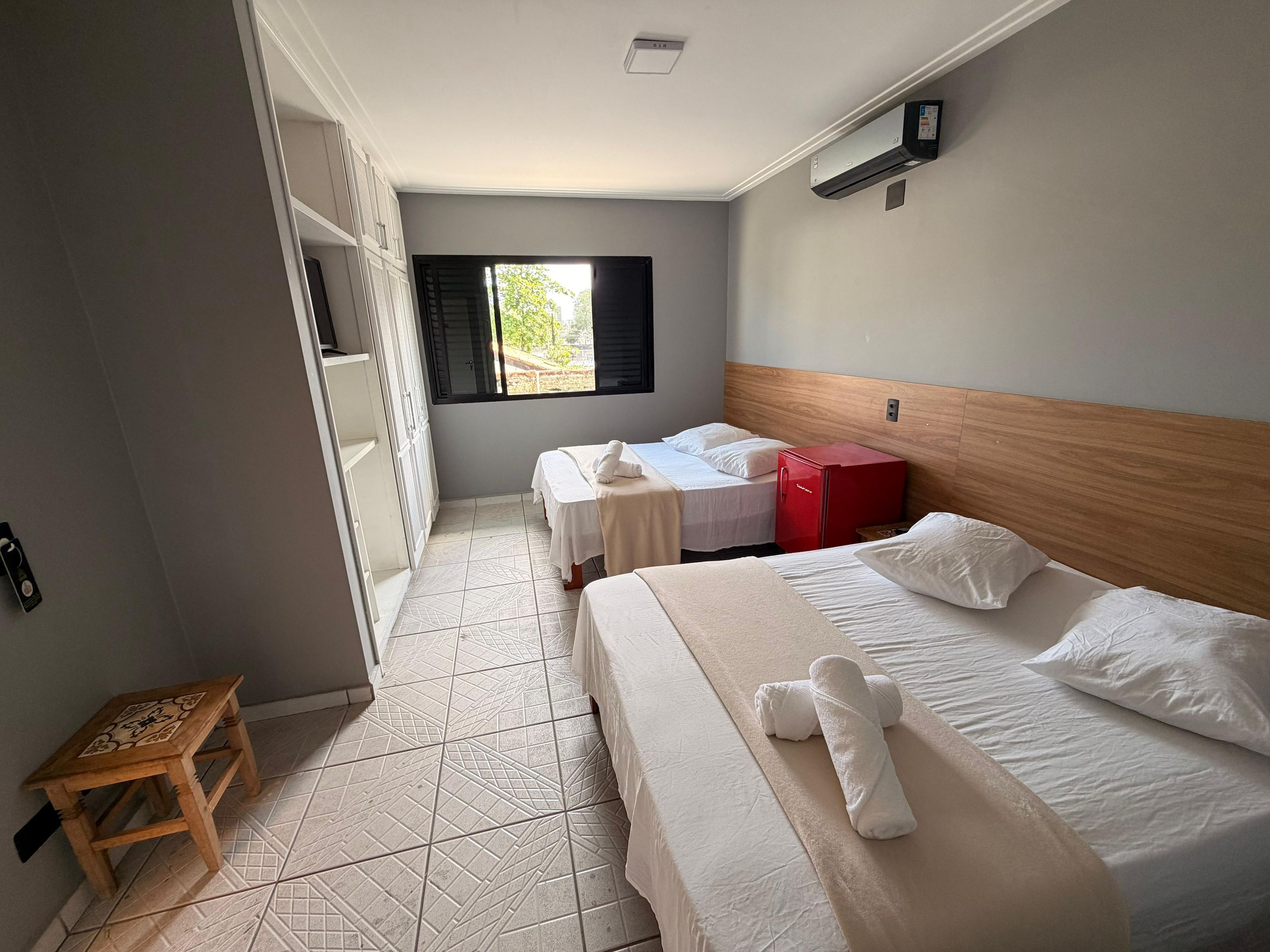 Habitación de hotel con dos camas, cabecera de madera, un armario rojo y una ventana con persianas.