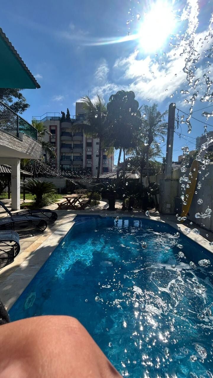 Una piscina con agua cristalina, rodeada de sillas de descanso y palmeras, con un edificio al fondo.