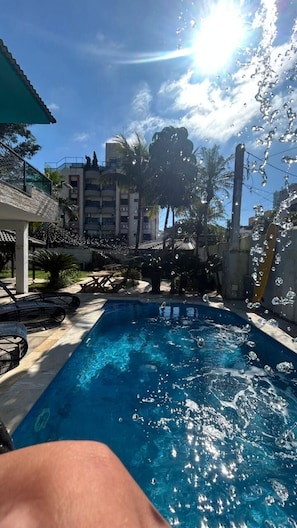 Una piscina con agua cristalina, rodeada de sillas de descanso y palmeras, con un edificio al fondo.