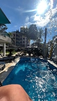 A swimming pool with clear water, surrounded by lounge chairs and palm trees, with a building in the background.