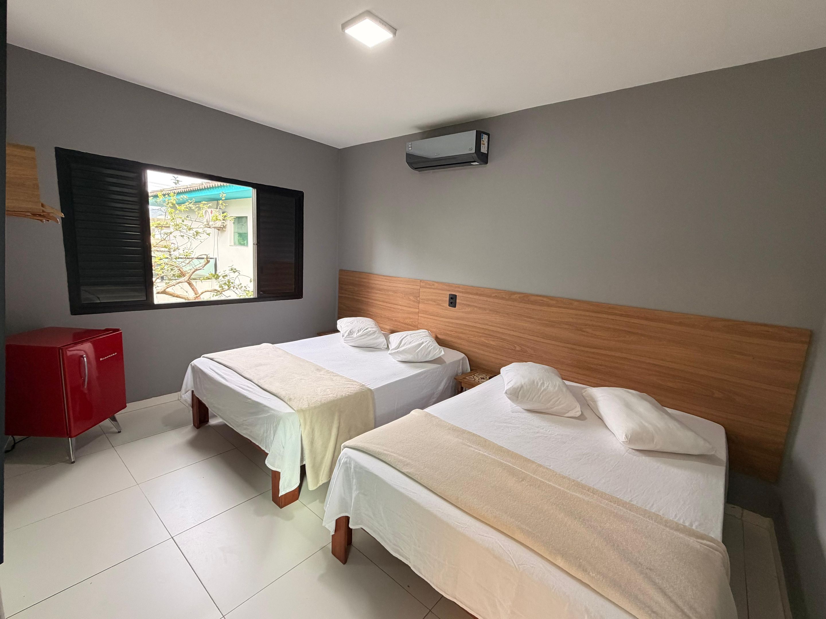 Habitación de hotel con dos camas, un minibár rojo y una ventana con persianas.