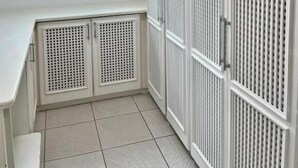A room with a white tiled floor, a white desk, a window with a view, and white lockers with a grid pattern. - Santa Rita Pousada (Guarujá)