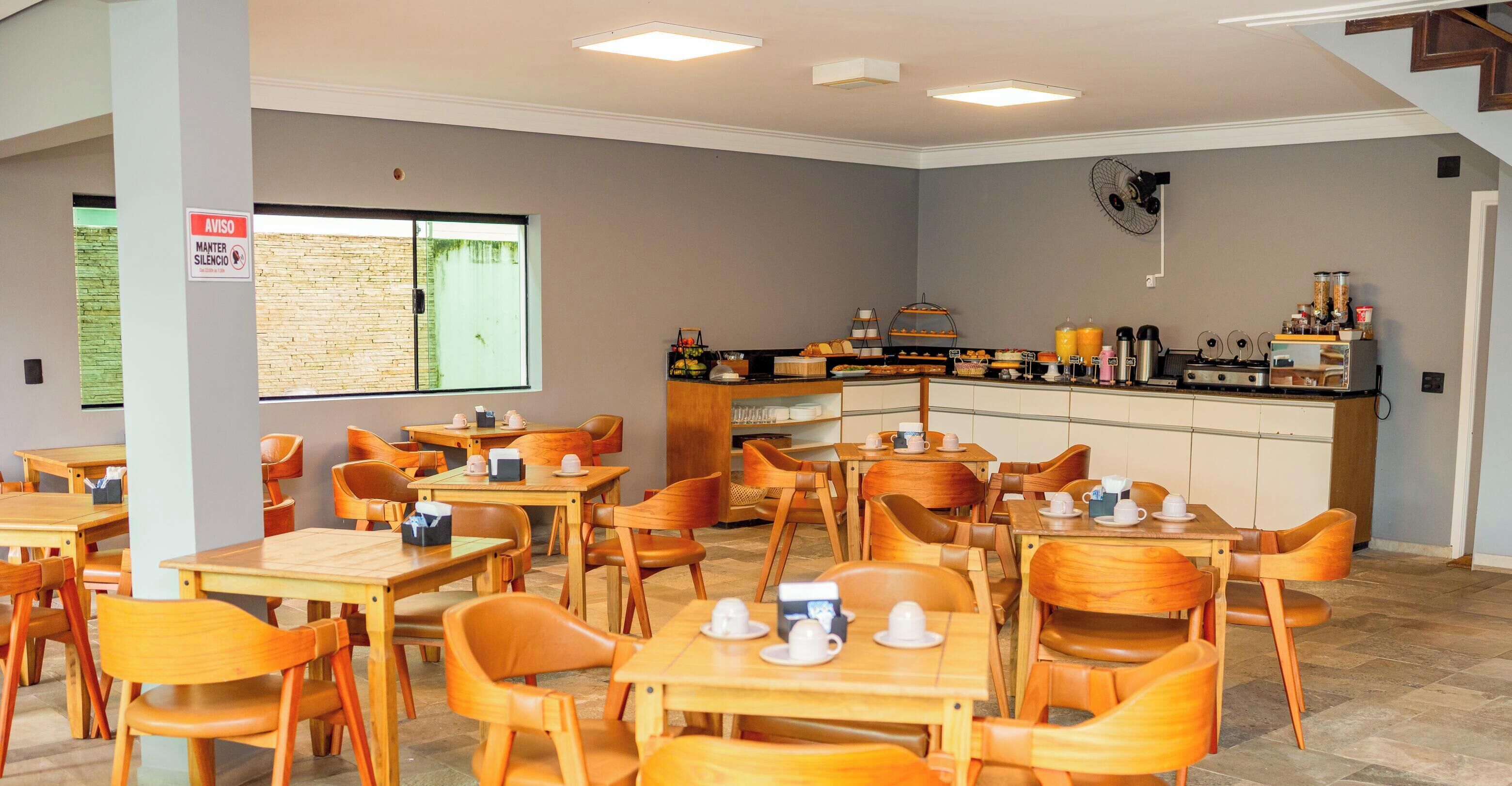 A cafe with wooden tables and chairs, a counter with food and drinks, and a sign on the wall.