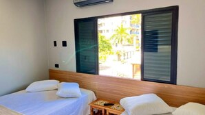 A hotel room with two beds, a small table, and a window with blinds.