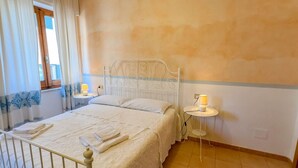 Un dormitori amb un llit, taulells laterals, una finestra amb cortines, i una paret amb un dibuix blau i blanc.