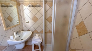 Un bany amb rentatge, mirall, prestatge per tovalloles i zona de dutxa.