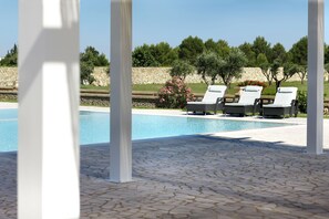 Un área de piscina con sillones de descanso y piso de baldosas de piedra.