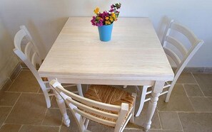 Una mesa de comedor con un jarrón azul de flores, rodeada de cuatro sillas blancas con asientos de mimbre.