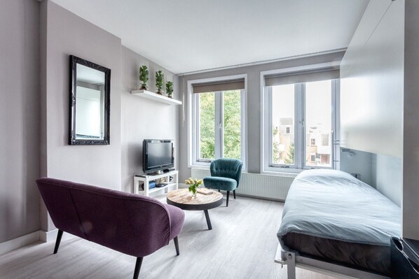 A modern bedroom with a bed, a TV, a purple chair, a blue chair, and a small table with plants.