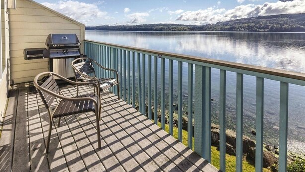 Eine Terrasse mit Grill und zwei Stühlen mit Blick auf einen stillen See.