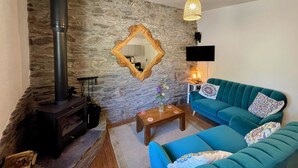 A living room with a stone wall, a fireplace, a sofa, a coffee table, and a hanging light fixture. - Mountain Retreat situated amongst the ruins of the old miners village (Allihies)