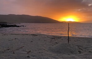 A beach with a sunset, rocky shoreline, and a stick in the sand.