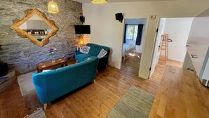 A cozy living room with a stone wall, a blue sofa, wooden flooring, and pendant lighting. - Mountain Retreat situated amongst the ruins of the old miners village (Allihies)