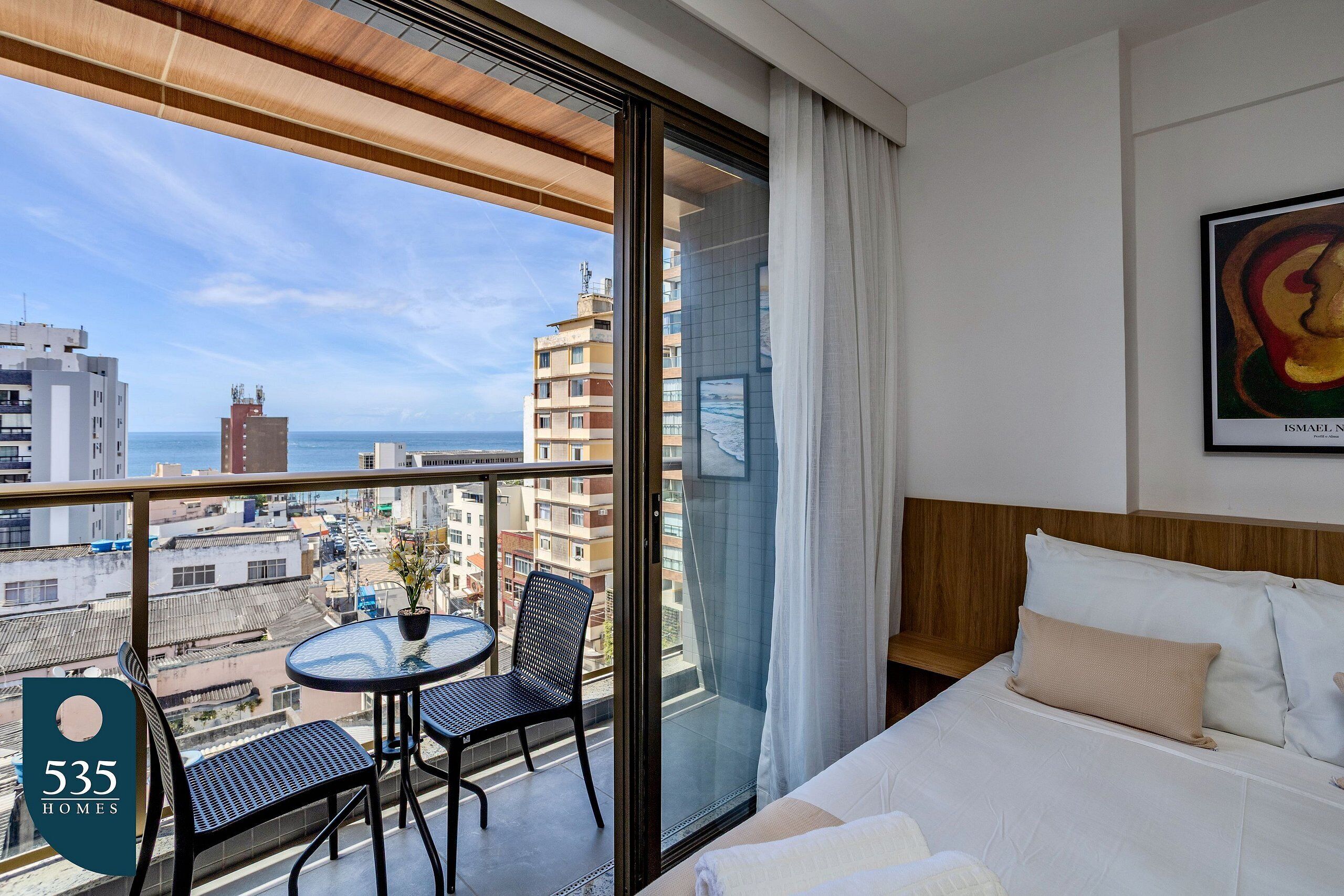 A hotel room with a balcony, a bed, a painting, and a view of the city and sea.