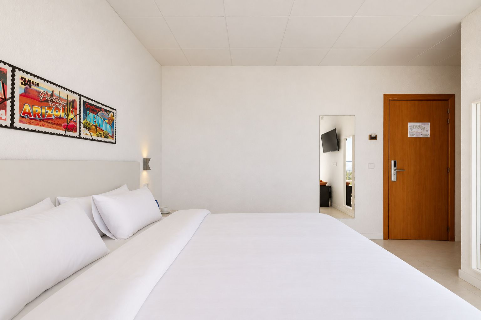 A hotel room with a large bed, a wall-mounted TV, a wooden door, and a window.