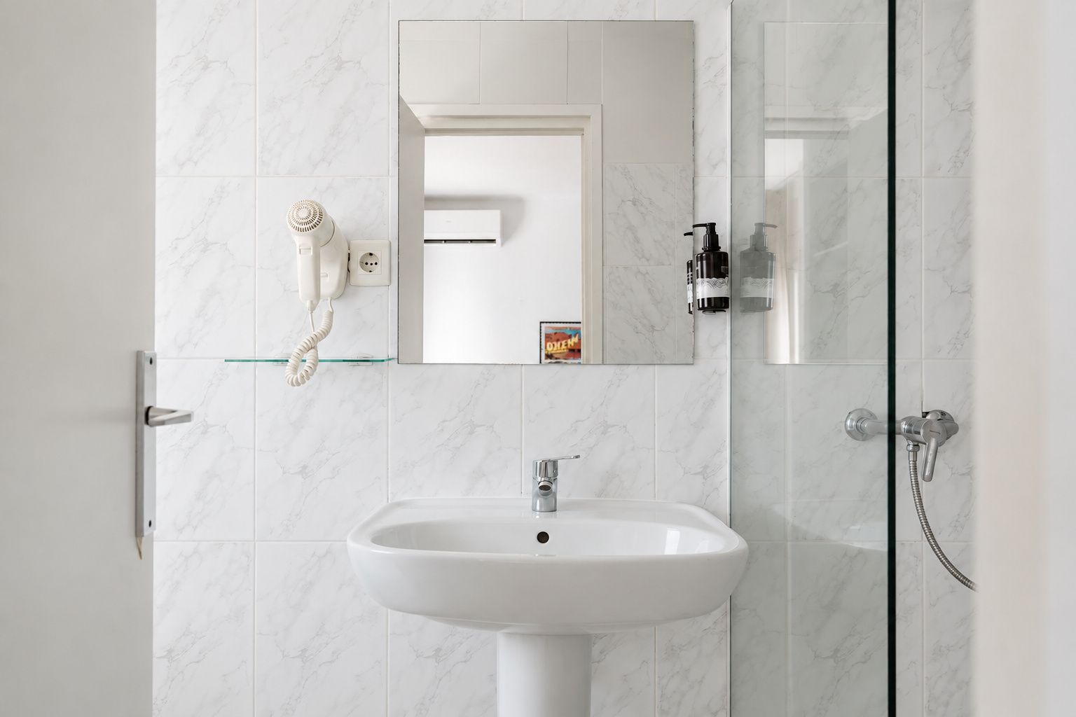 Un baño con lavamanos blanco, un espejo, secador de pelo de mano y ducha.