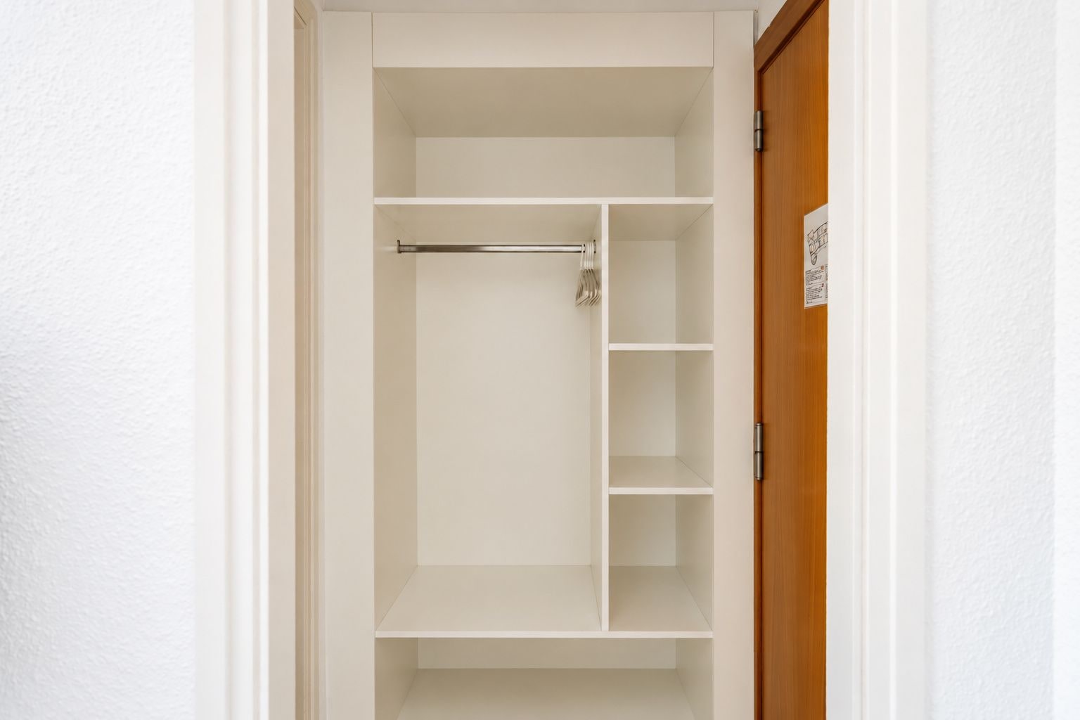 Ein begehbarer Kleiderschrank mit offenen Regalen, einer Kleiderstange und einer Tür mit Beschriftung.
