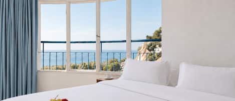 A hotel room with a large bed, a bowl of fruit, and a view of the sea.