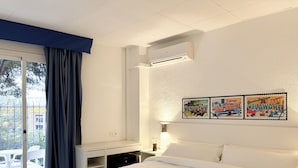 Hotelkamer met een bed, bureau, stoel, raam met gordijnen, airconditioning en een muur met drie ansichtkaarten.
