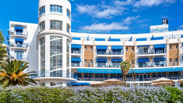 Een hotel met meerdere verdiepingen, balkons, een centraal torentje en een bord met de tekst 'Hotel de Vegas'.