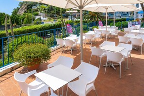 An outdoor patio with white tables and chairs, a potted plant, and a blue railing. - Las Vegas Hotel (Calella)