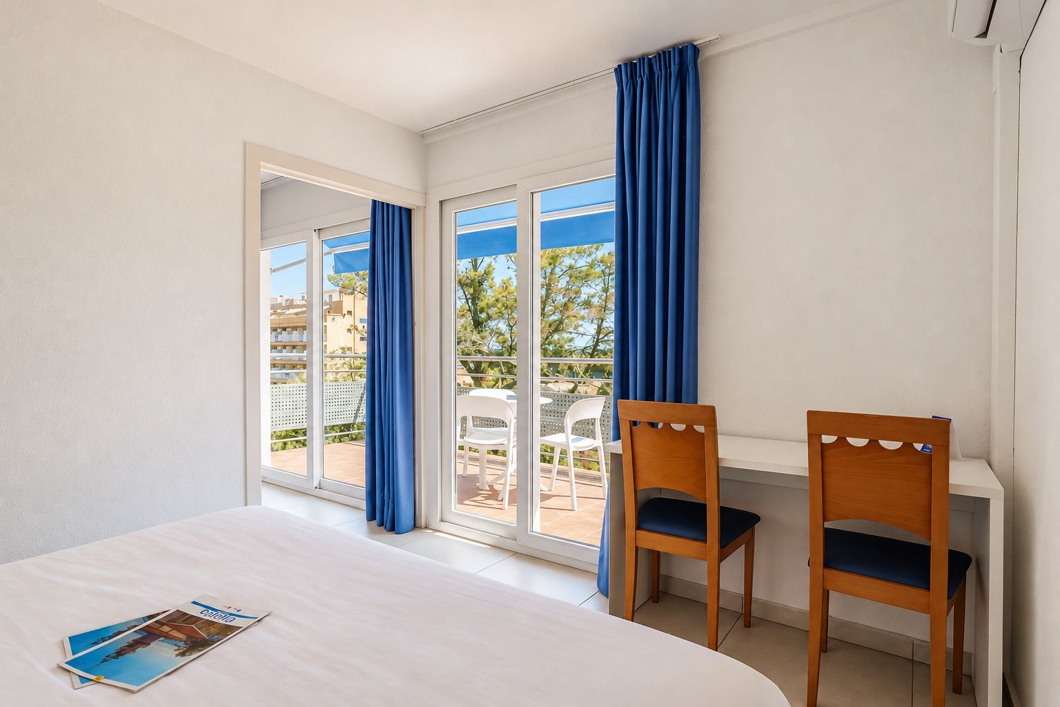 A hotel room with a bed, two chairs, a window with curtains, and a view of the outside.