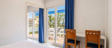 A hotel room with a bed, two chairs, a window with curtains, and a view of the outside.