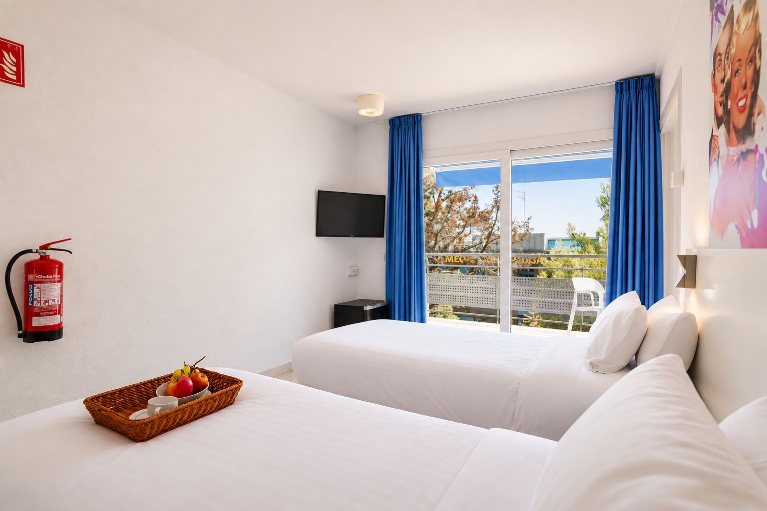 Habitación de hotel con dos camas, un extintor, un televisor y una ventana con cortinas azules.
