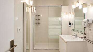 A modern bathroom with a glass-enclosed shower, a vanity with a sink, and a hairdryer mounted on the wall.