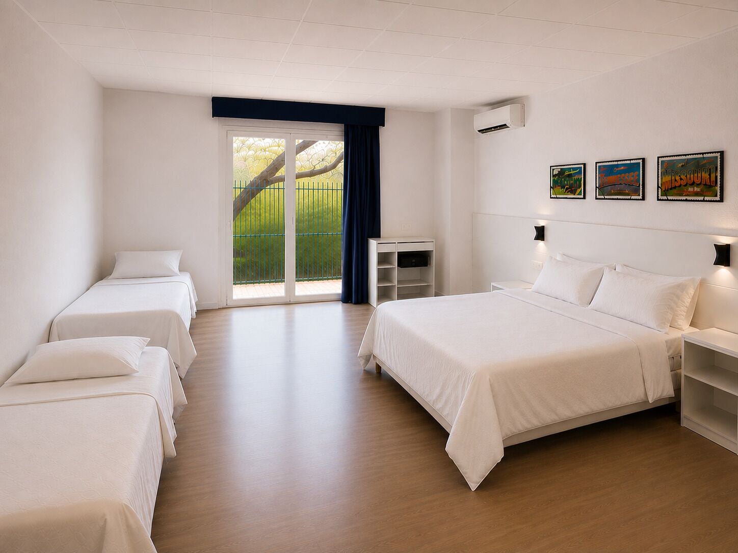 A hotel room with a large bed, two smaller beds, a desk, and a sliding glass door to the outside.