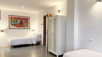 Een hotelkamer met twee bedden, een kledingkast, een wandlamp en een poster van een stadsgezicht.
