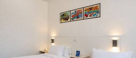 Habitación de hotel con dos camas individuales, una mesita de noche con una taza y una lámpara de pared.