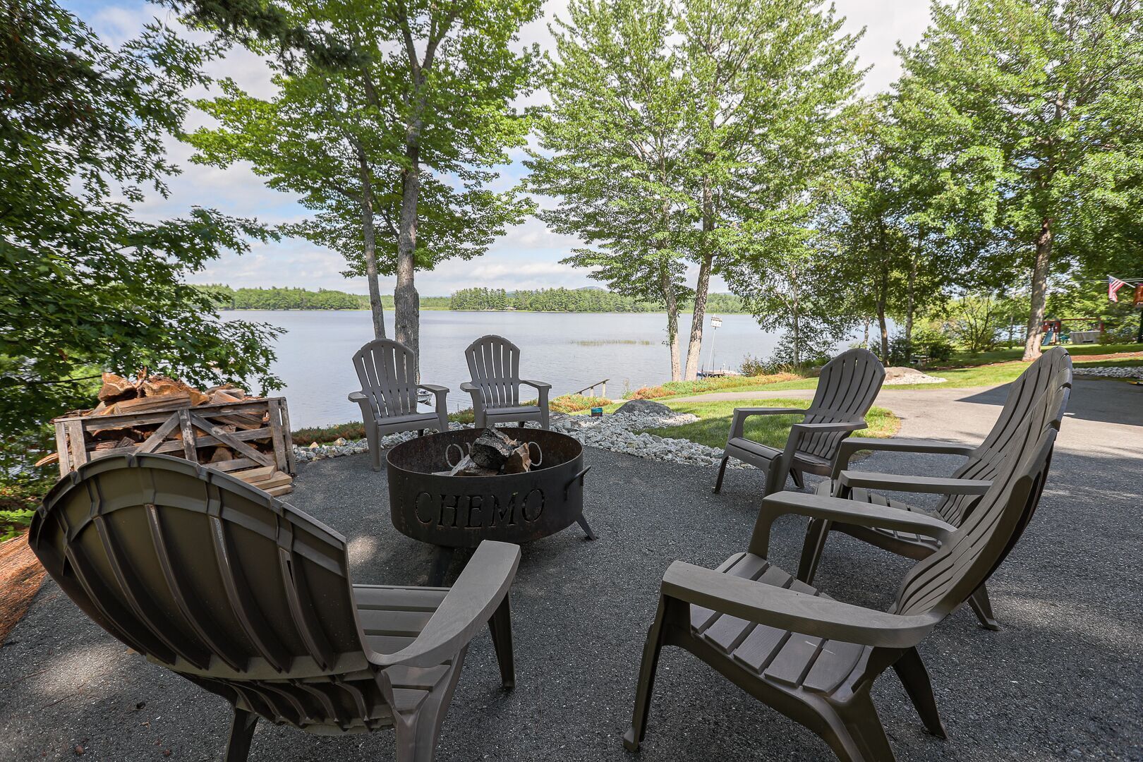 Een terras met Adirondack-stoelen, een vuurplaats en uitzicht op een meer.
